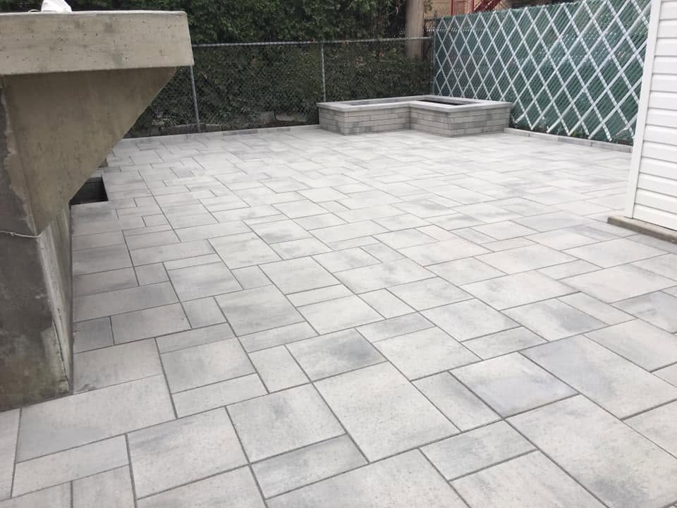 Patio arrière en pavé uni grand format avec muret et jardinière en pierre